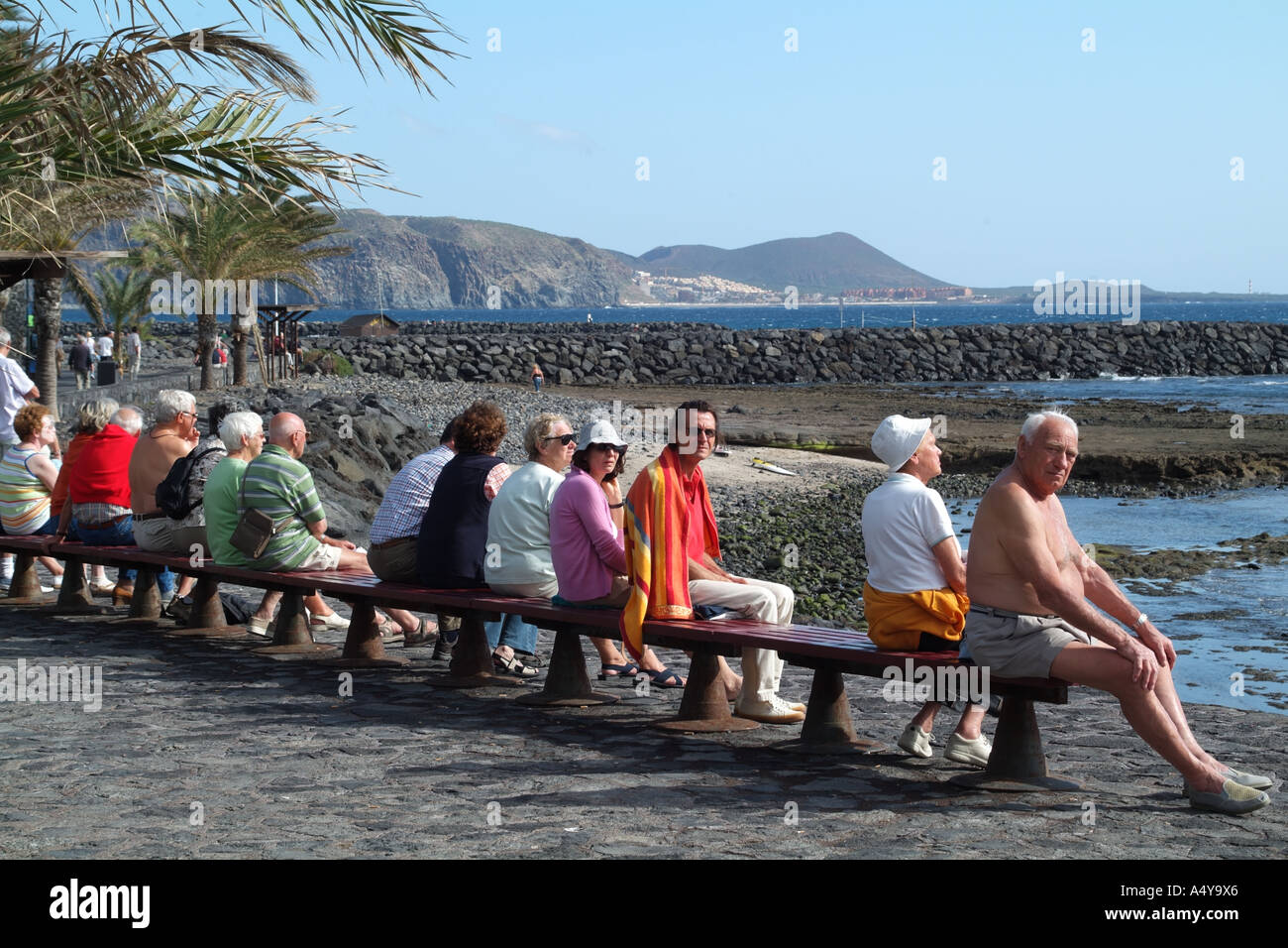 Sunbathers sitting on bench Las Americas le sud de Tenerife Espagne Banque D'Images