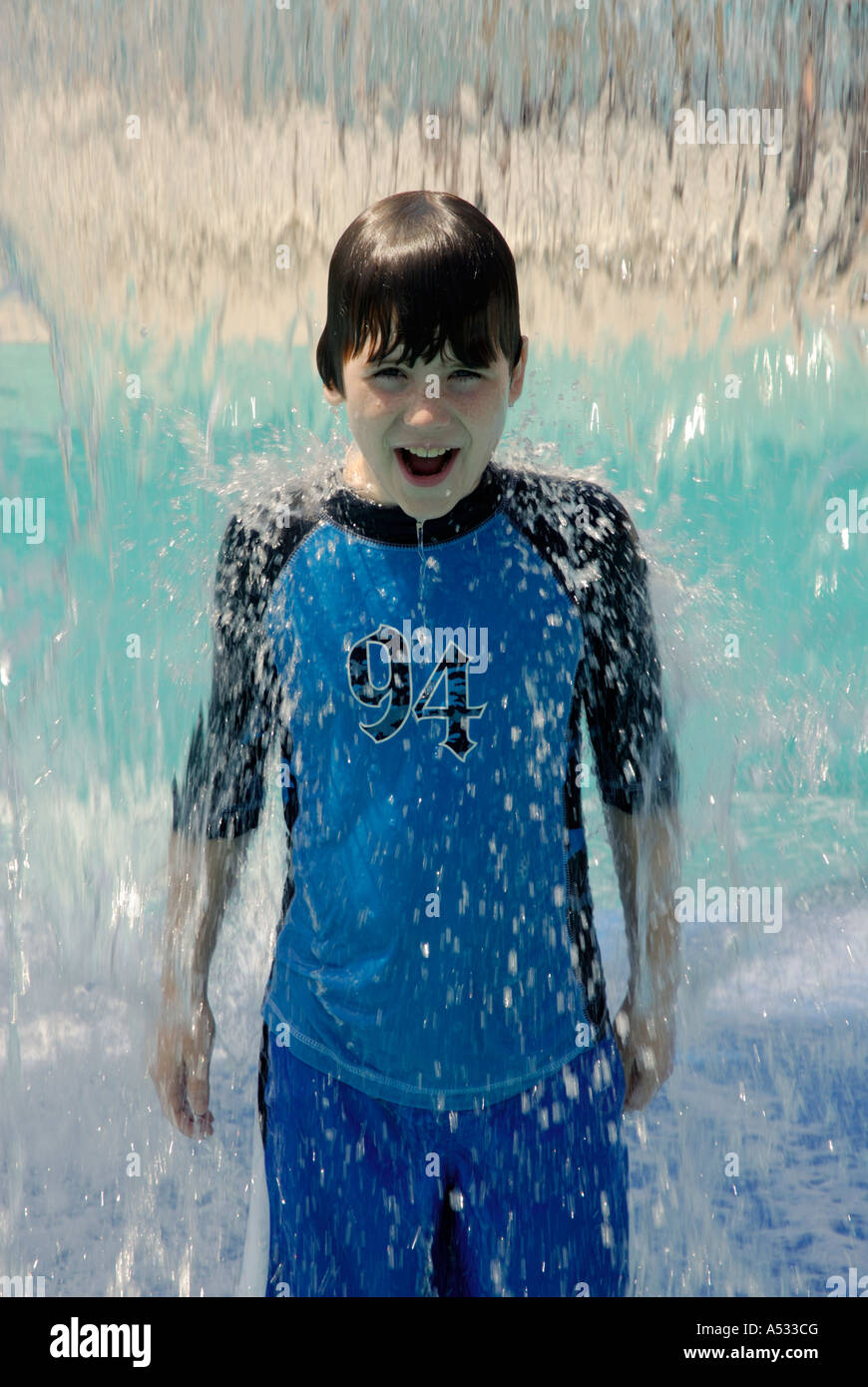Young boy smiling in chute d'eau de refroidissement à l'arrêt cascade jeux pour enfants en été. Propriétés de l'eau. L'eau est un puissant evapor Banque D'Images
