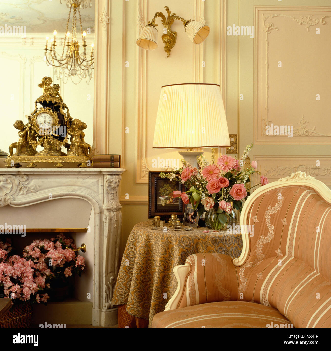 Chaise de style français de pêche et de table avec bande de tissu pêche voyant derrière la cheminée de marbre avec horloge baroque doré sur la cheminée Banque D'Images