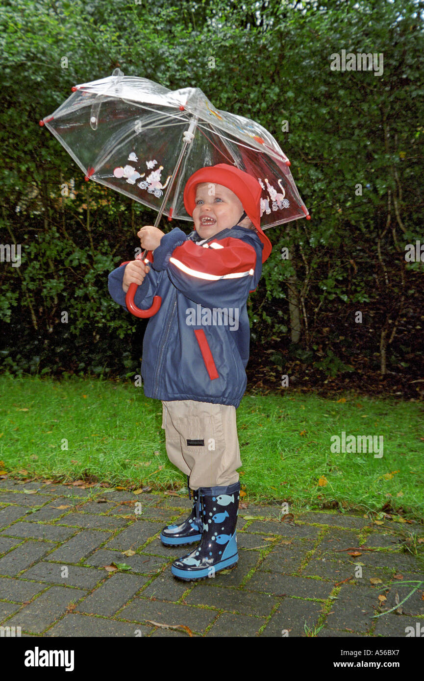 Petite fille habillée d'un imperméable est titulaire d'un parasol et de rires Allemagne Banque D'Images