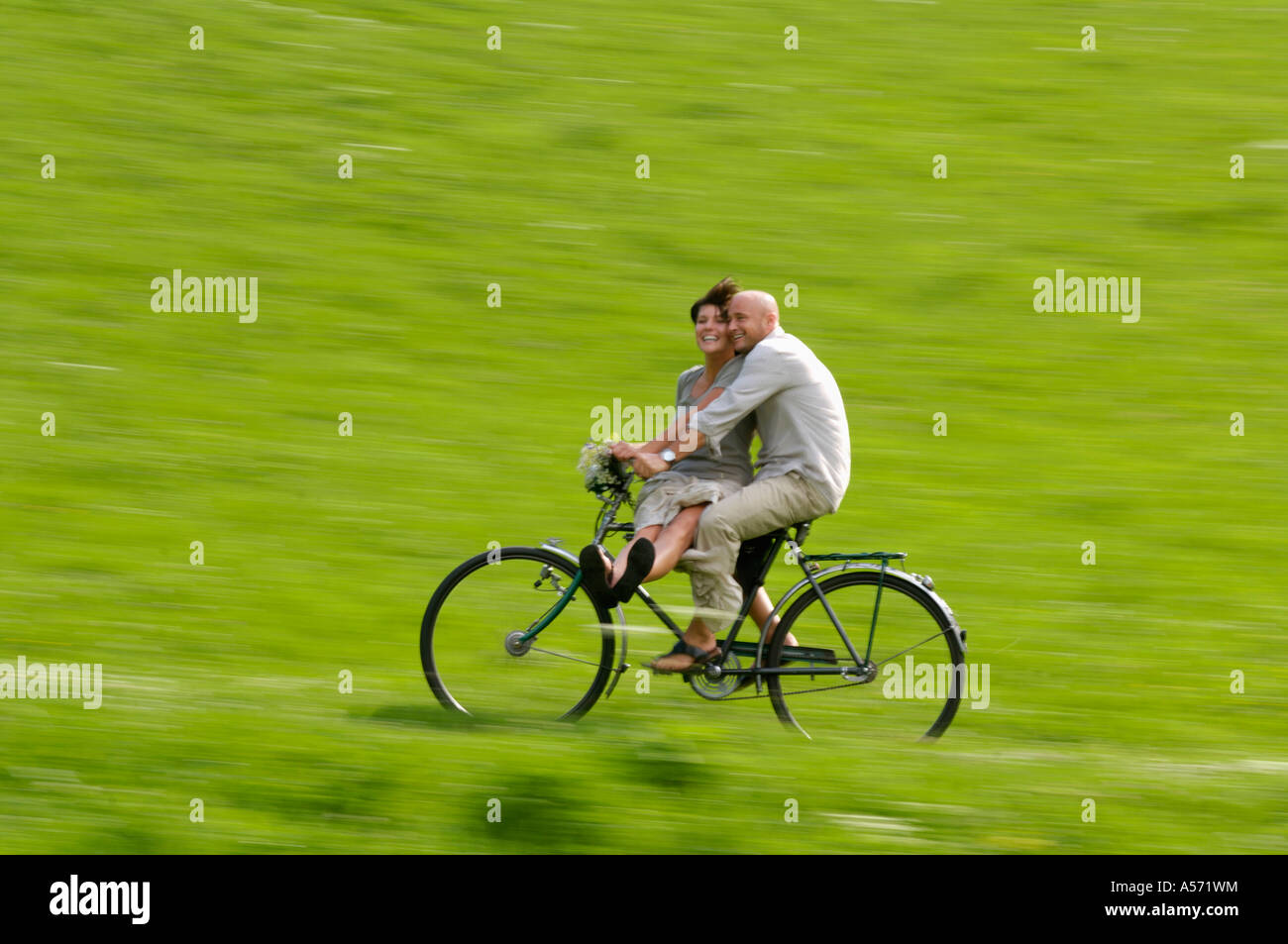 Couple riding bicycle in meadow Banque D'Images