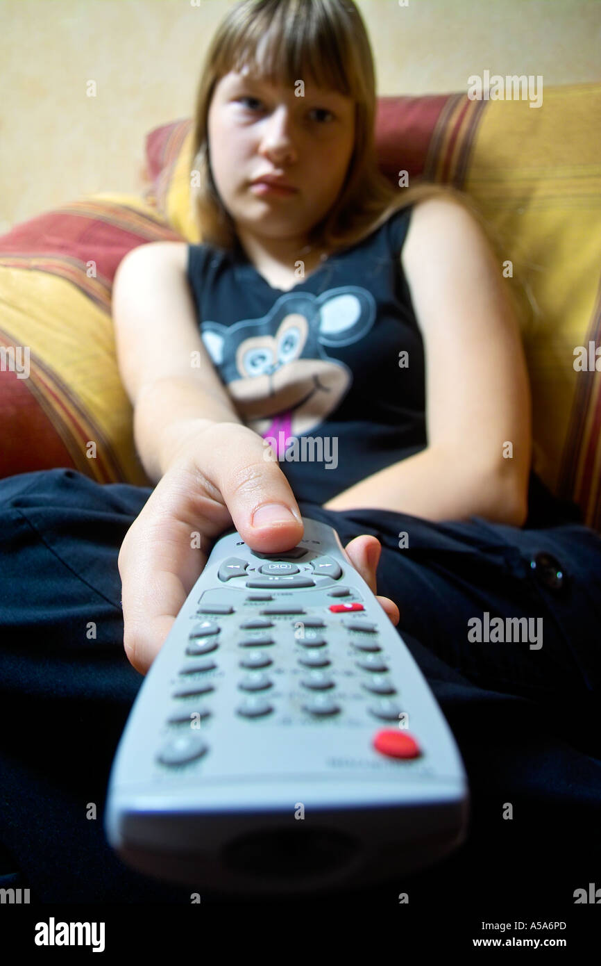 Teenage girl regarder la TV avec la télécommande dans sa main channel renversant le téléphage Banque D'Images