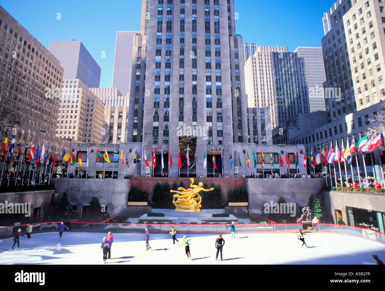 Patinoire et patineurs du Rockefeller Center de New York. 30 Rockefeller Plaza et bâtiments environnants. Drapeaux internationaux volant à Midtown Manhattan Banque D'Images