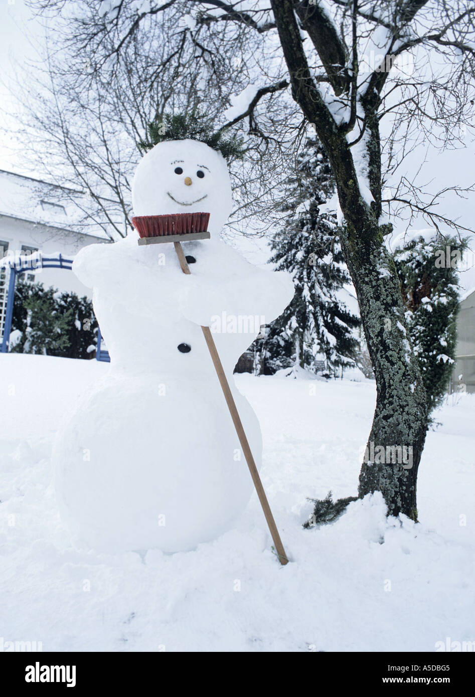 Le Snowman holding broom par arbre nu Banque D'Images