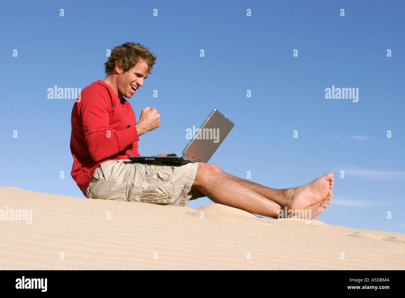 Homme assis sur le sable dans le désert avec ordinateur portable, clenching fist Banque D'Images