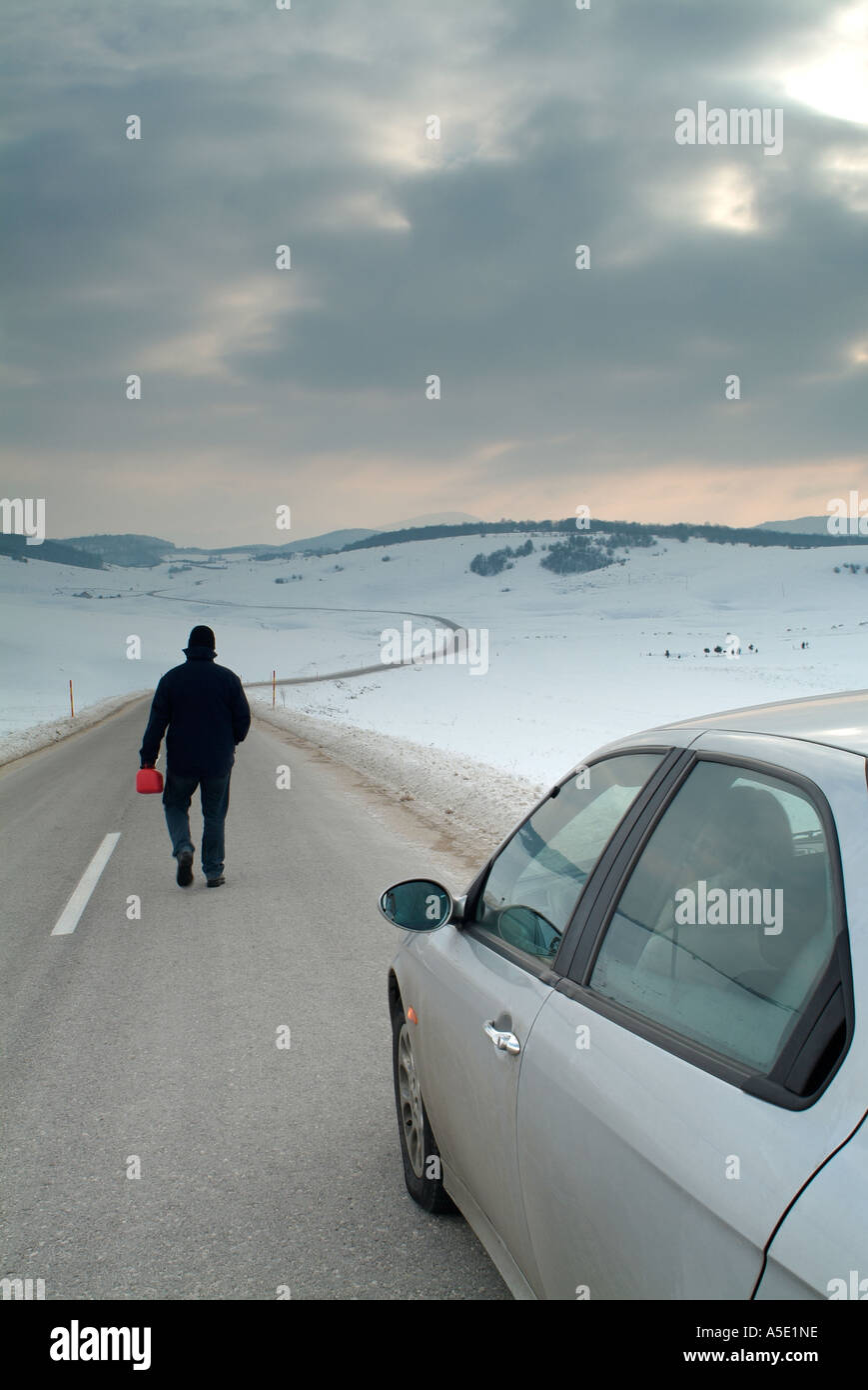 Homme quitte son conjoint dans la voiture pour marcher le long d'une route isolée dans une vallée couverte de neige à la recherche de carburant Banque D'Images