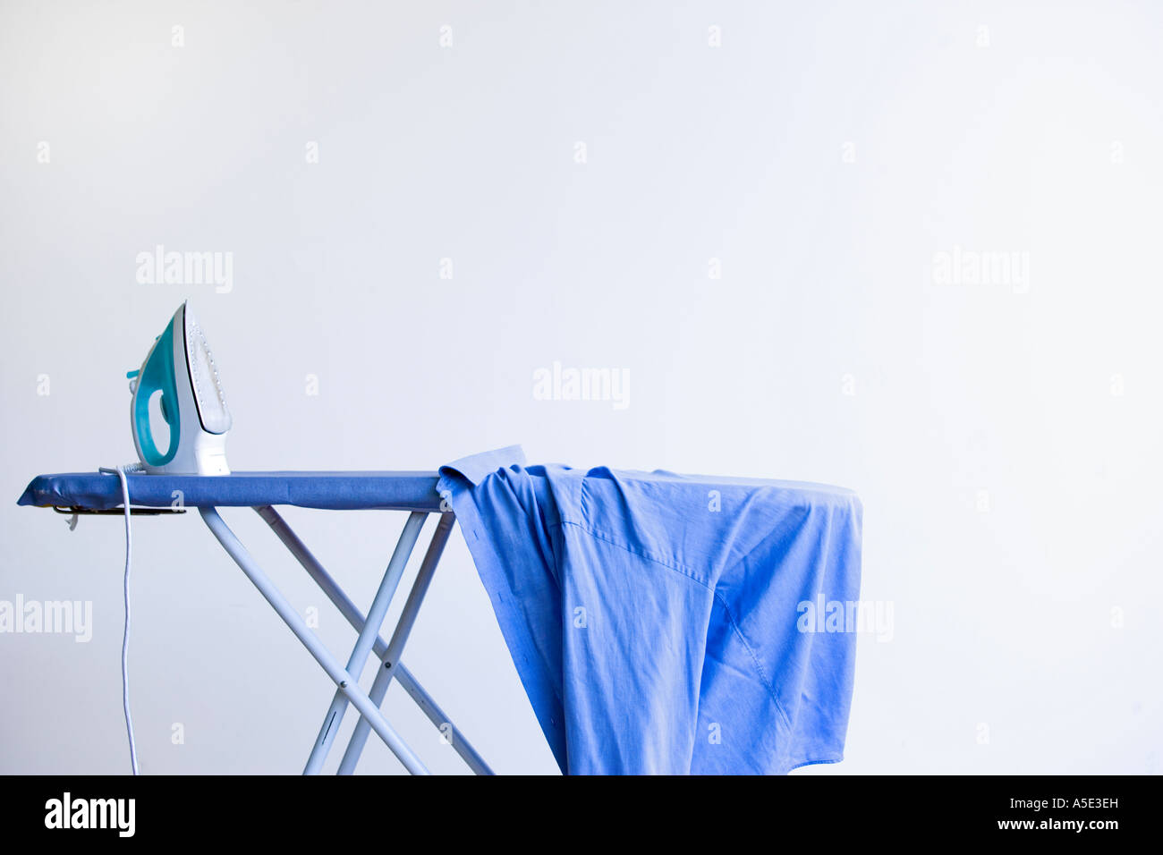 Fer à repasser sur une planche à repasser avec chemise bleue Banque D'Images