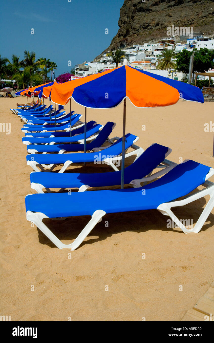 Orange et bleu parasols et transats sur la plage de Puerto de Mogan, Grande Canarie, Îles Canaries, Espagne. Banque D'Images