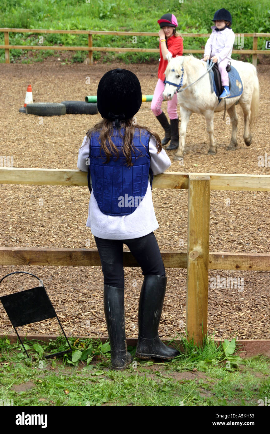 9 ans, fille de matériel d'équitation à plus de clôture à l'école d'équitation à une petite fille d'être dirigé sur un poney Banque D'Images