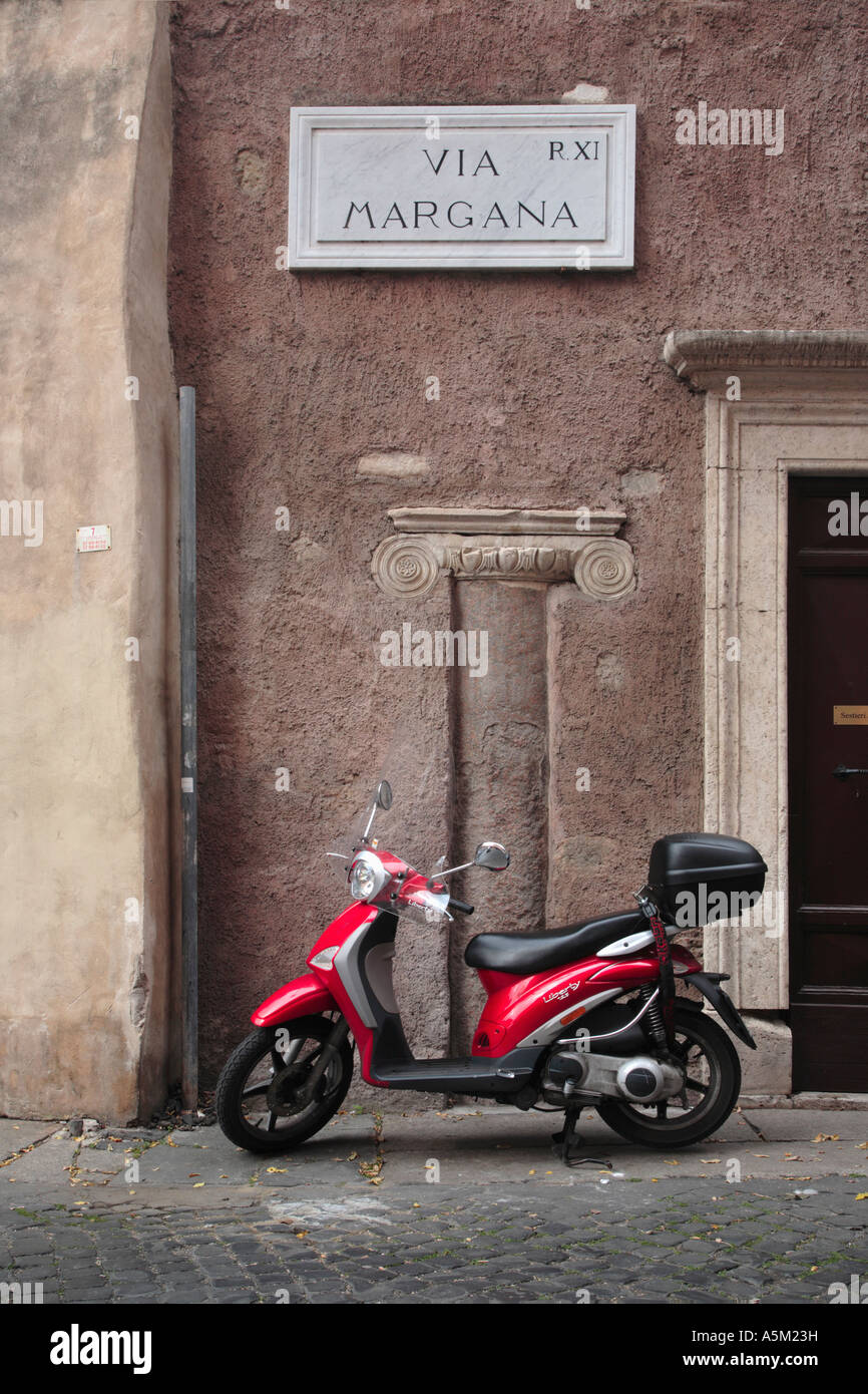 Cyclomoteur rouge garée devant un morceau d'architecture romaine encastré dans le mur sur une rue de Rome Italie Banque D'Images