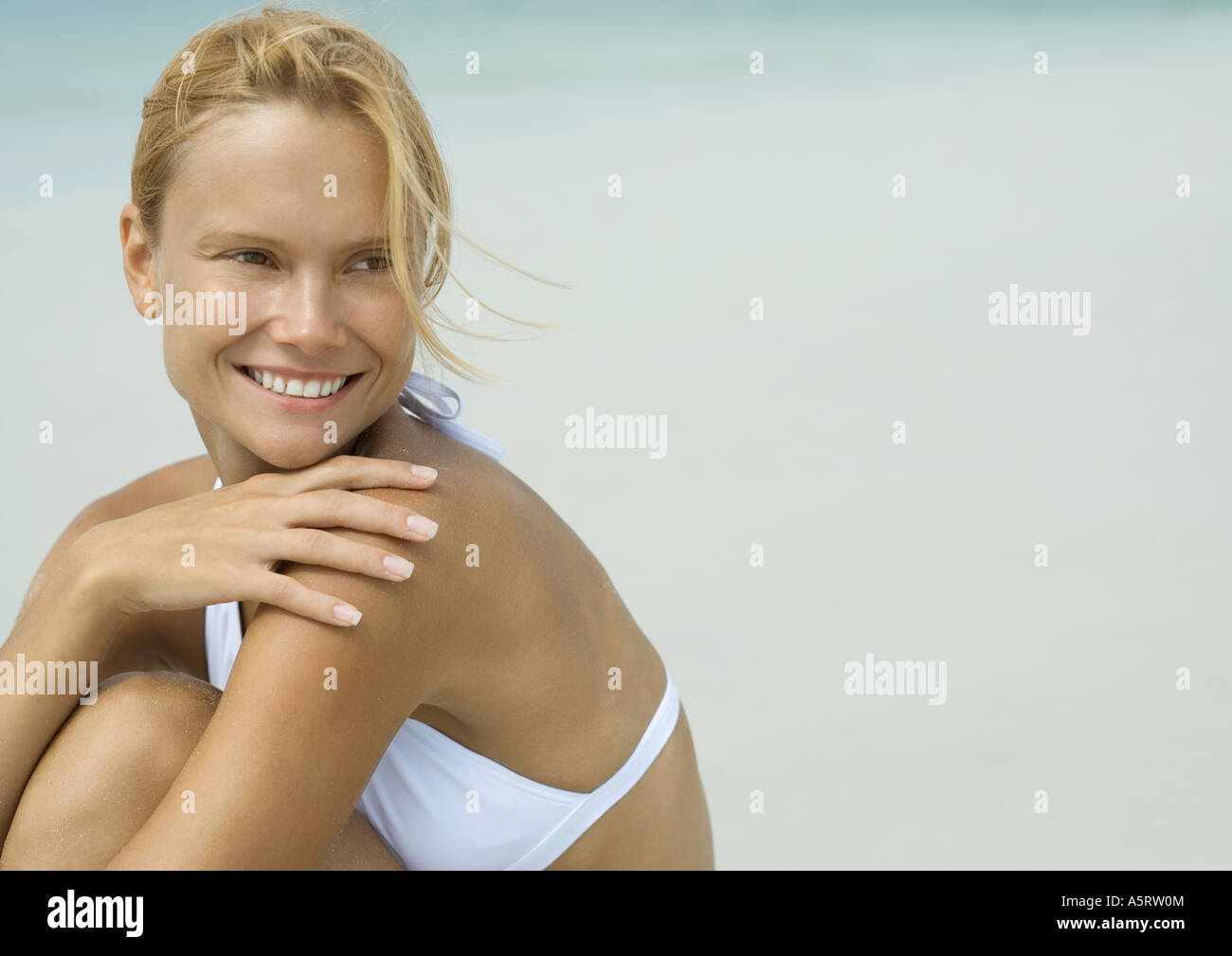 Woman in bikini sitting on beach with hand on shoulder Banque D'Images