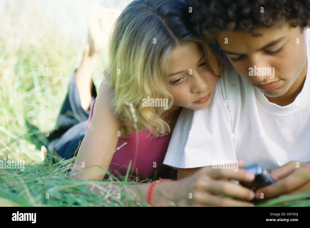 Boy and girl lying in grass, looking at cell phone Banque D'Images