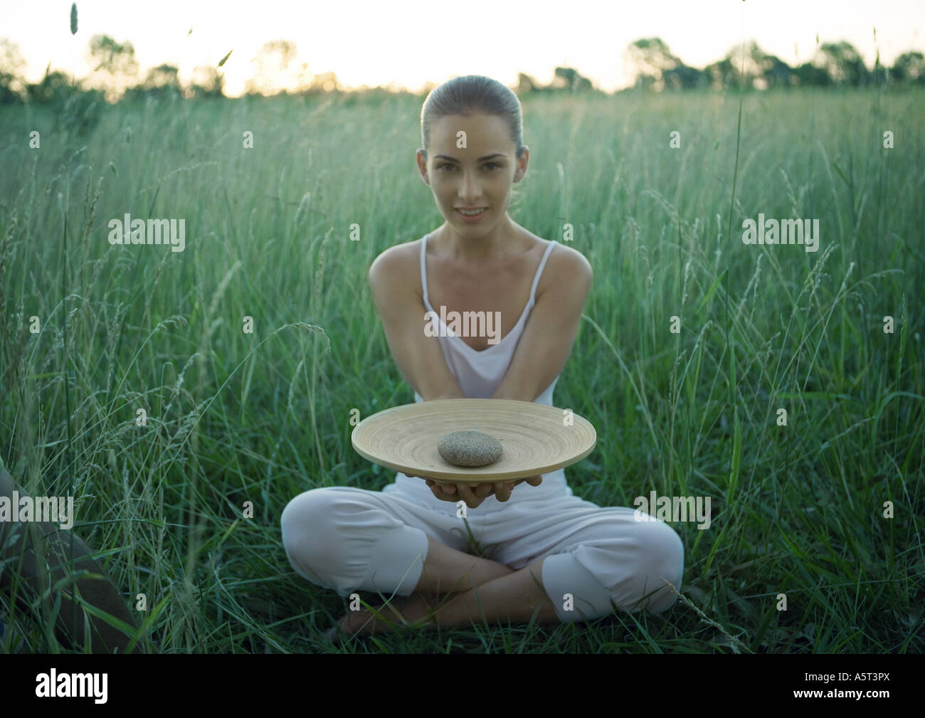 Woman sitting in field, holding out bol contenant stone Banque D'Images