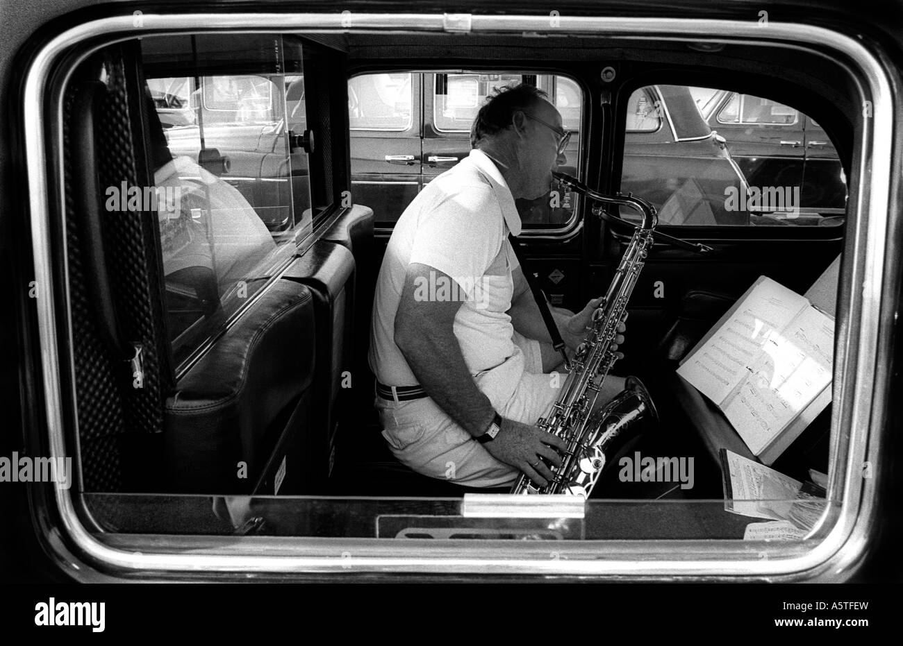 Un chauffeur de taxi Londres jouant le saxaphone dans l'arrière de son taxi dans l'attente à l'aéroport de Heathrow. Banque D'Images