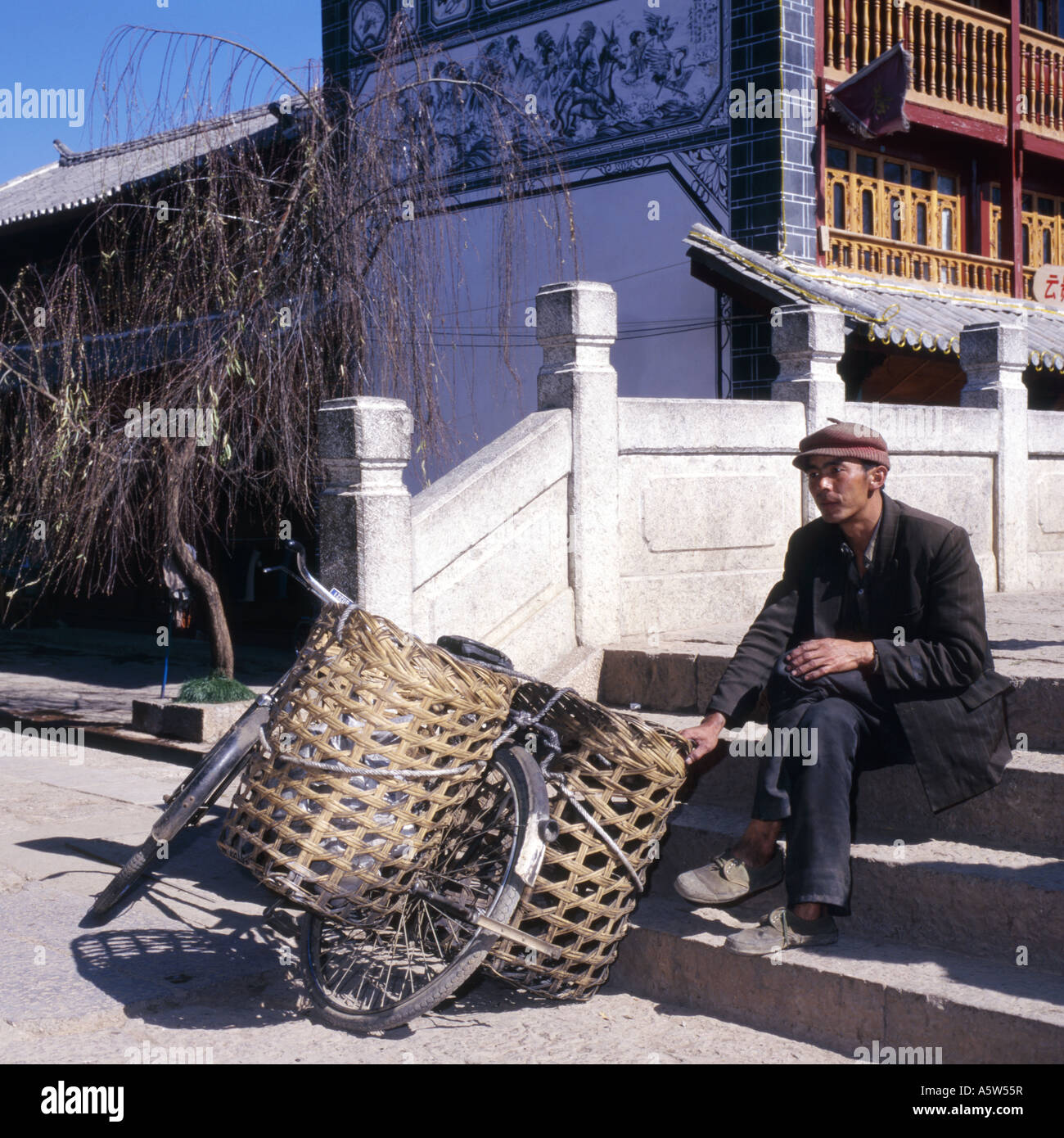 Homme de la région de vieux vêtements,assis près d'un vélo traditionnel,par le carré à Lijiang, Yunnan Province, China. Banque D'Images