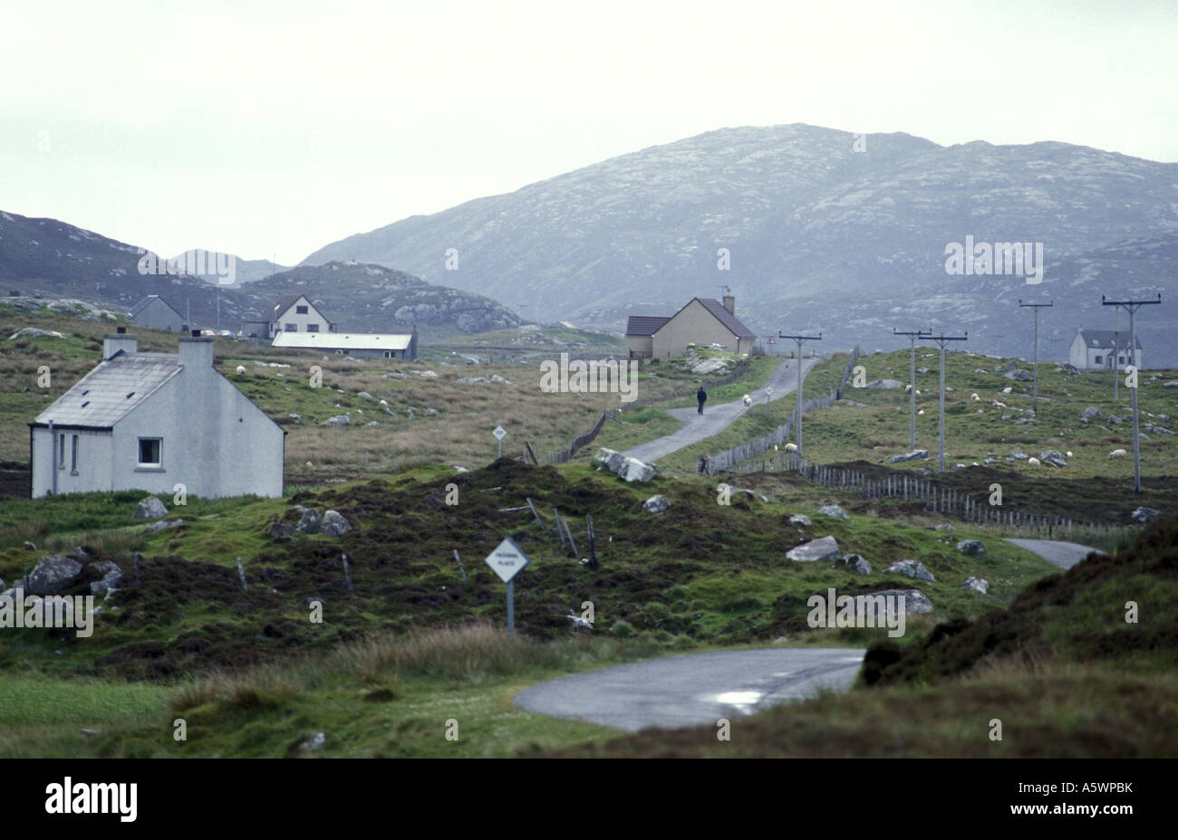 Homme marchant sur une route rurale parsemée de logement dans l'île de South Uist Ecosse Banque D'Images