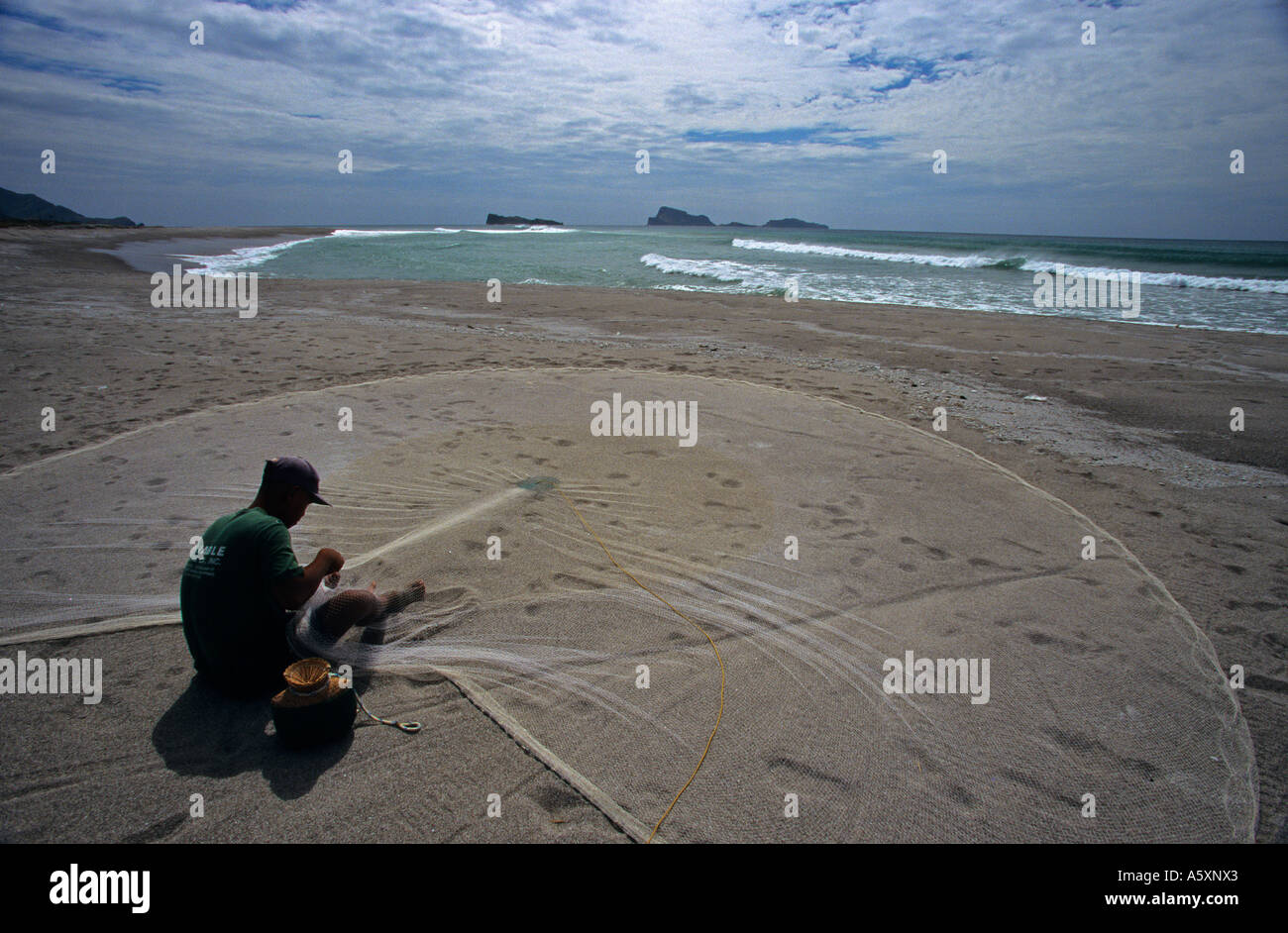 Sam pêcheur réparant son casting net sur la plage de San Miguel. Pêcheur assis raccommodant fils épervier sur la plage de San Miguel. Banque D'Images