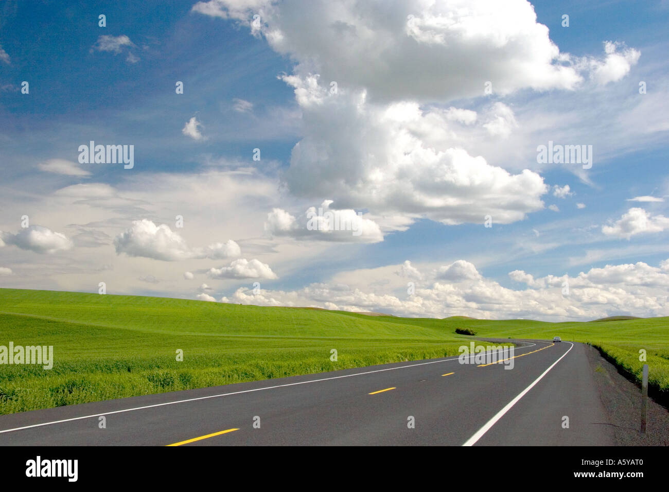 Une autoroute dans l'est du Washington coupe à travers une exploitation de blé avec des collines et des nuages. Banque D'Images
