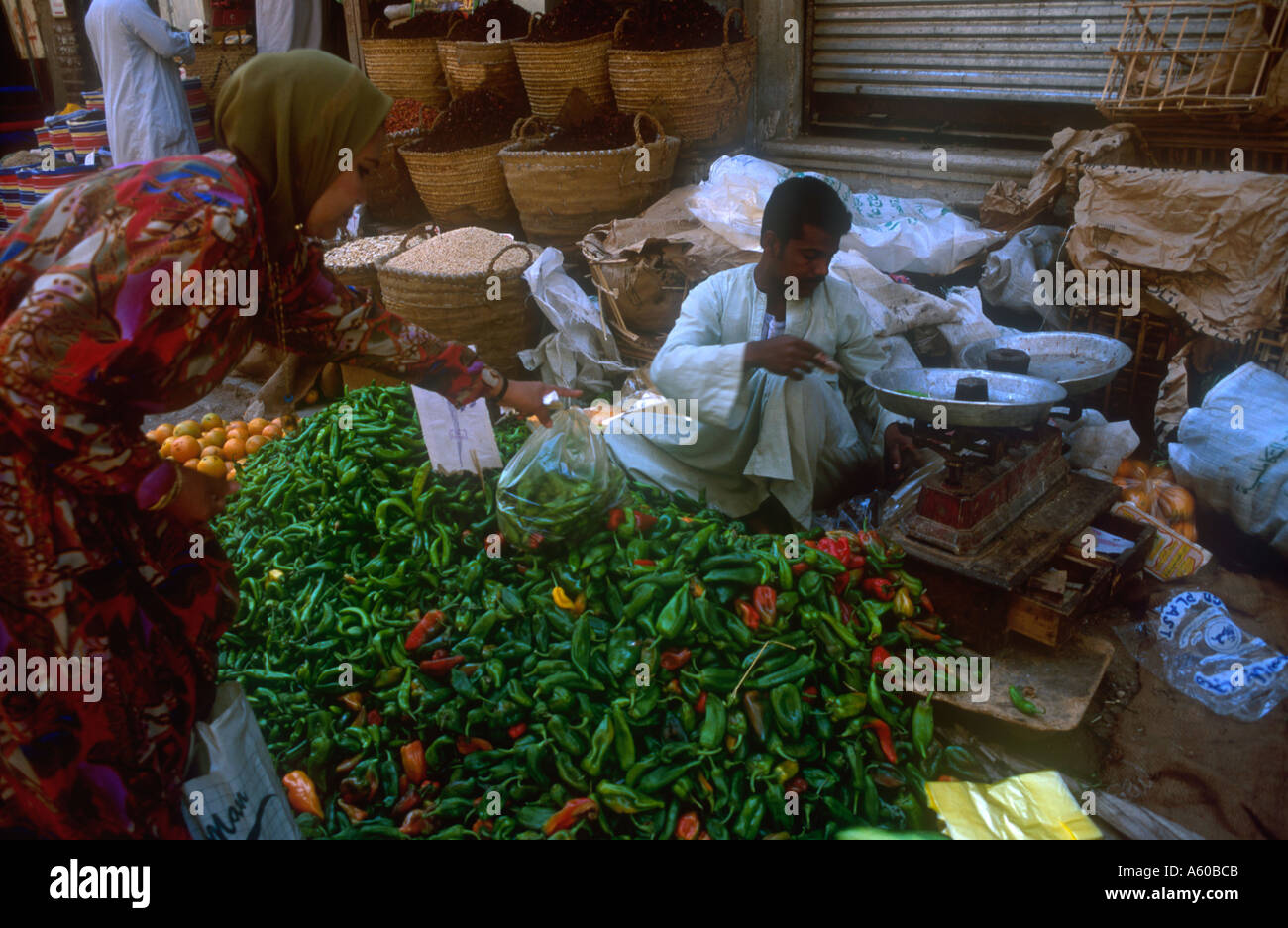 La Haute Egypte Egypte Louxor Woman Buying green chili peppers dans un marché de rue avec le vendeur d'un poids certains poivrons sur scales Banque D'Images