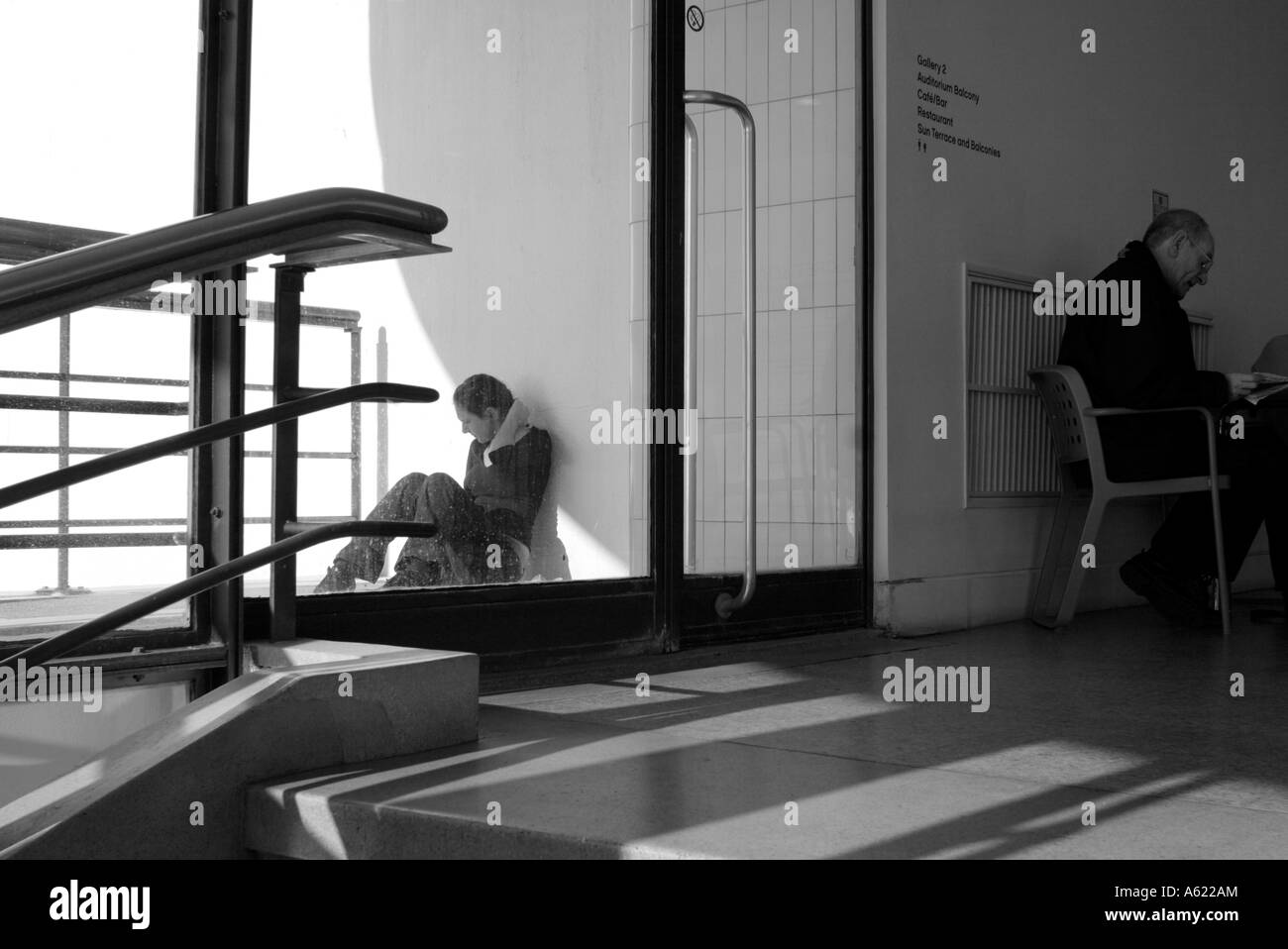 L'homme assis sur une chaise et de la lecture à l'intérieur avec teenage girl sitting on sol à l'extérieur Banque D'Images