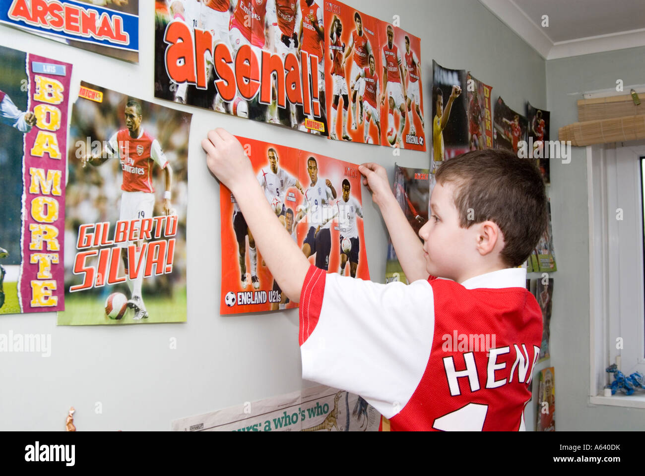 Jeune garçon supporter de football d'Arsenal en posant des affiches sur le mur de sa chambre, London, England, UK Banque D'Images