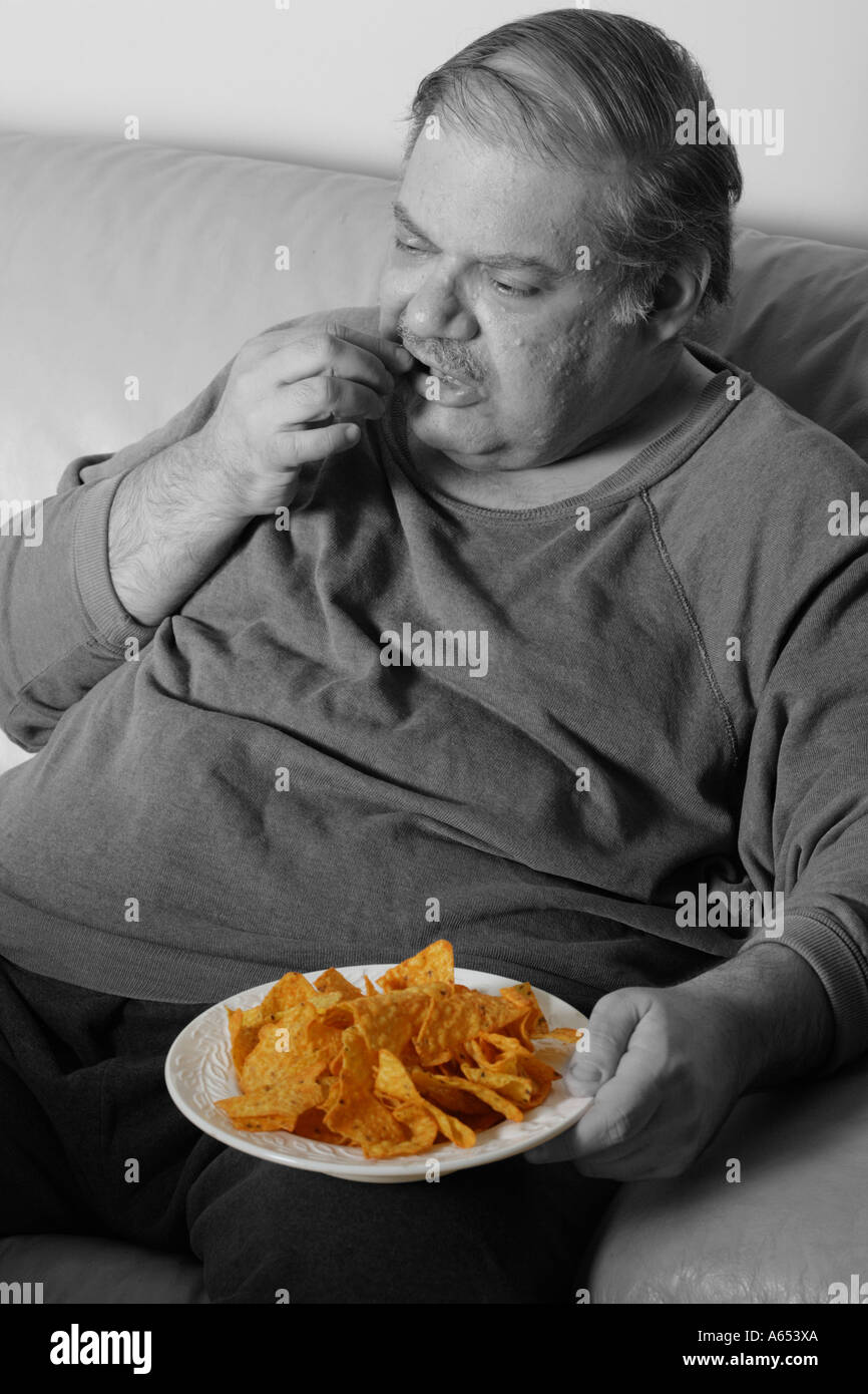 Homme mange un excès de plaquettes alors qu'assis sur son canapé à la maison. Banque D'Images