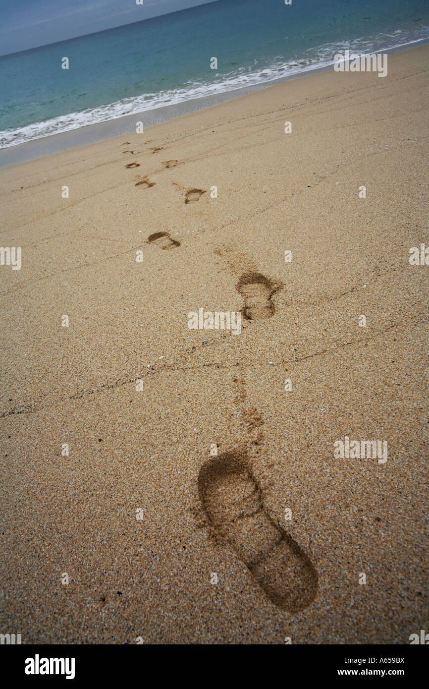 Des traces de pas dans le sable sur une plage disparaissant dans la mer Banque D'Images