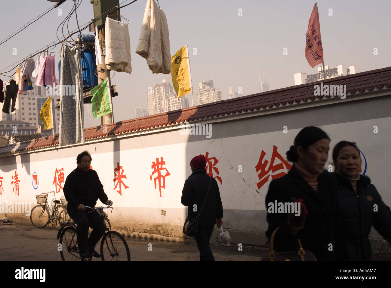 Blanchisserie plane sur la rue pour sécher comme passant passer devant un mur recouvert de caractères chinois, Shanghai, Chine Banque D'Images