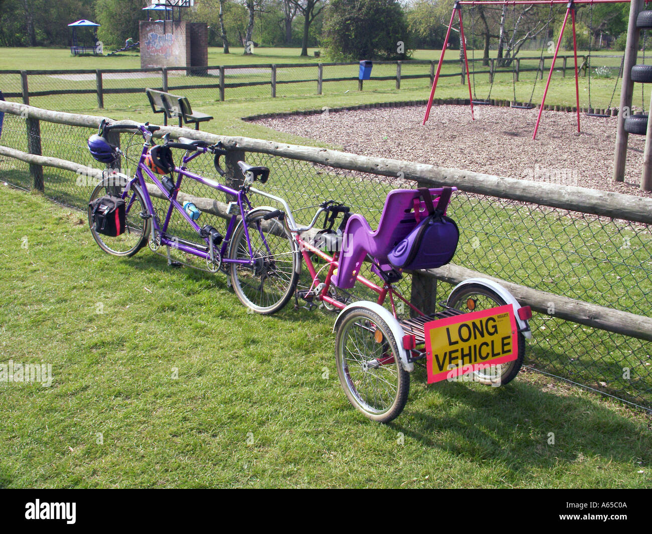Tandem vélo long véhicule signe sur le vélo famille vélo vélo siège enfant garé à côté de l'aire de jeux pour enfants balançoires le jour d'été à Brentwood Essex Angleterre Banque D'Images