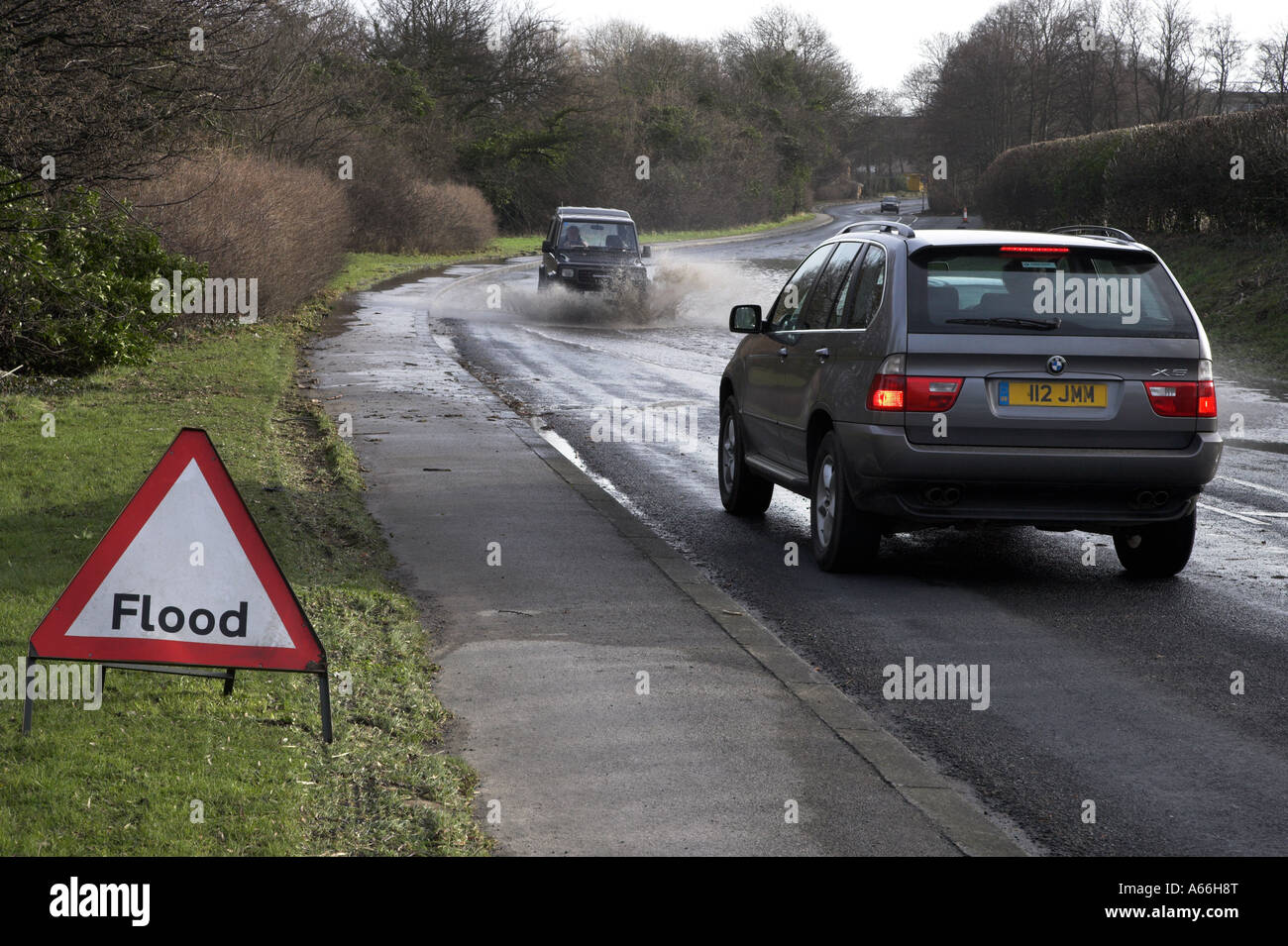Plaque de signalisation triangulaire au passage des véhicules, les projections et l'attente à conduire, par des eaux d'inondation de la route bloquant - près de Otley, West Yorkshire, Royaume-Uni. Banque D'Images