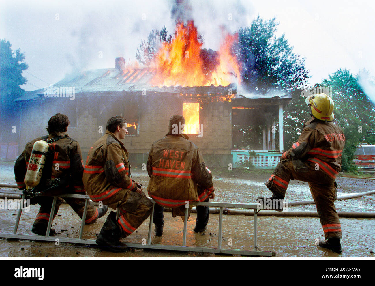 Les pompiers humour regardant une maison brûler comme ils se détendre Banque D'Images