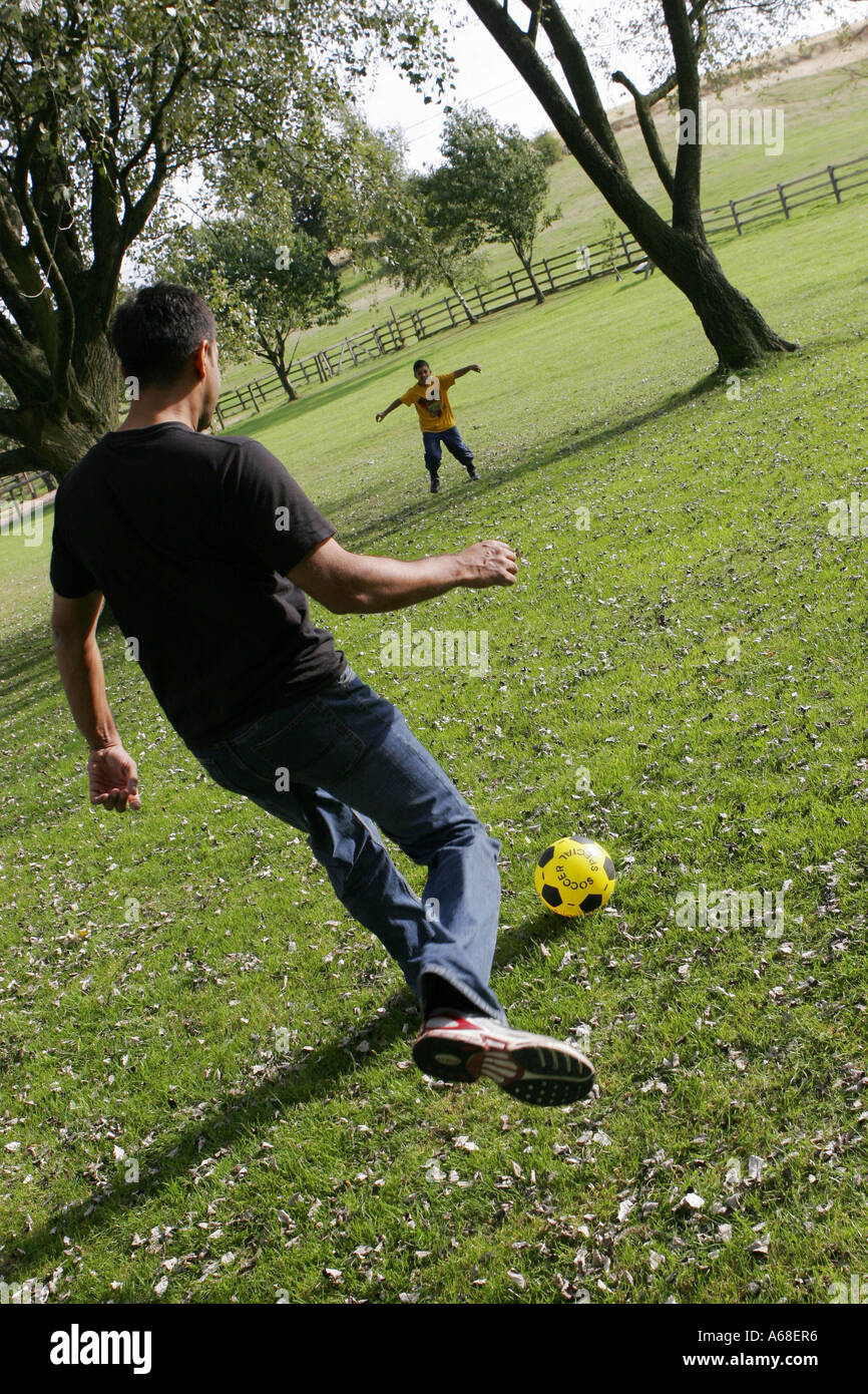 Père et fils asiatique jouant au football dans la campagne anglaise Banque D'Images
