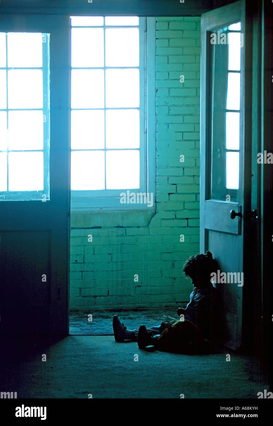 Petit enfant assise seule dans la sombre sale couloir d'un immeuble délabré Banque D'Images