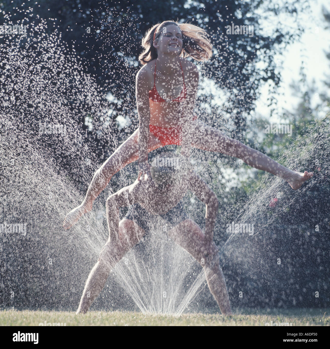 Adolescents jouant à saute-water sprinkler Banque D'Images