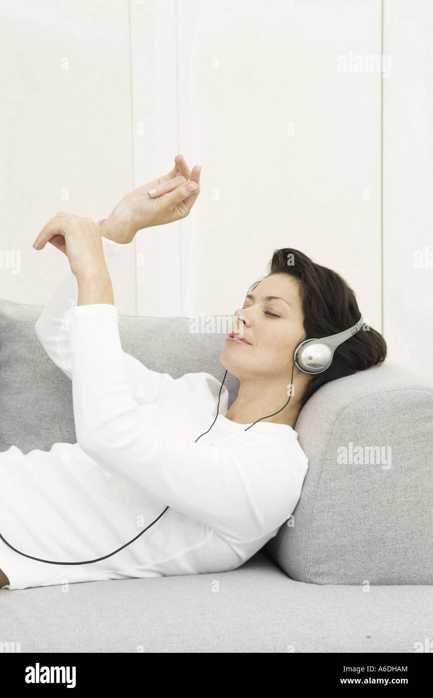 Portrait of a young woman wearing headphones listening to music on a couch Banque D'Images