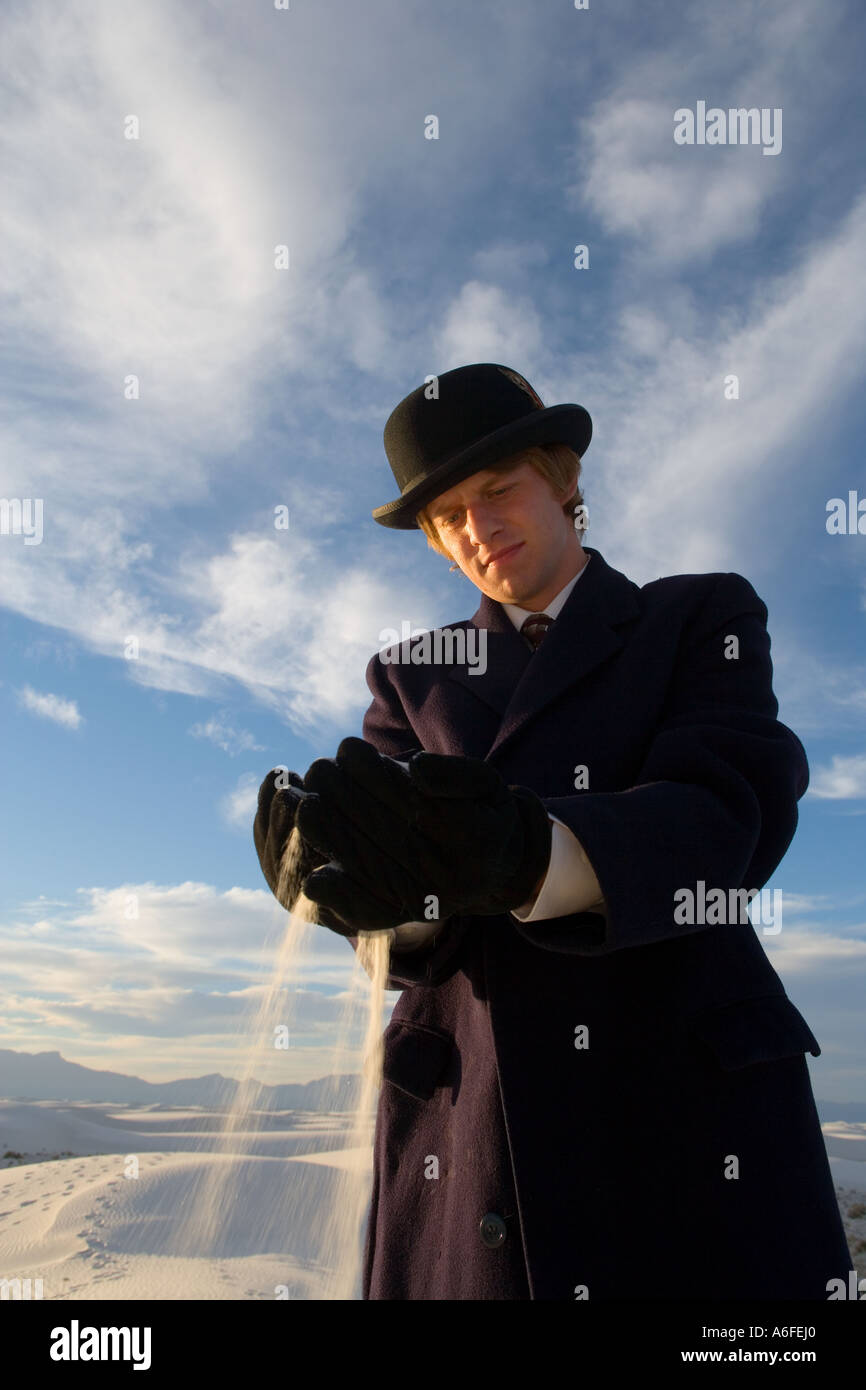 Homme portant chapeau melon et pardessus de sable blanc tenant dans ses mains dans le désert Banque D'Images