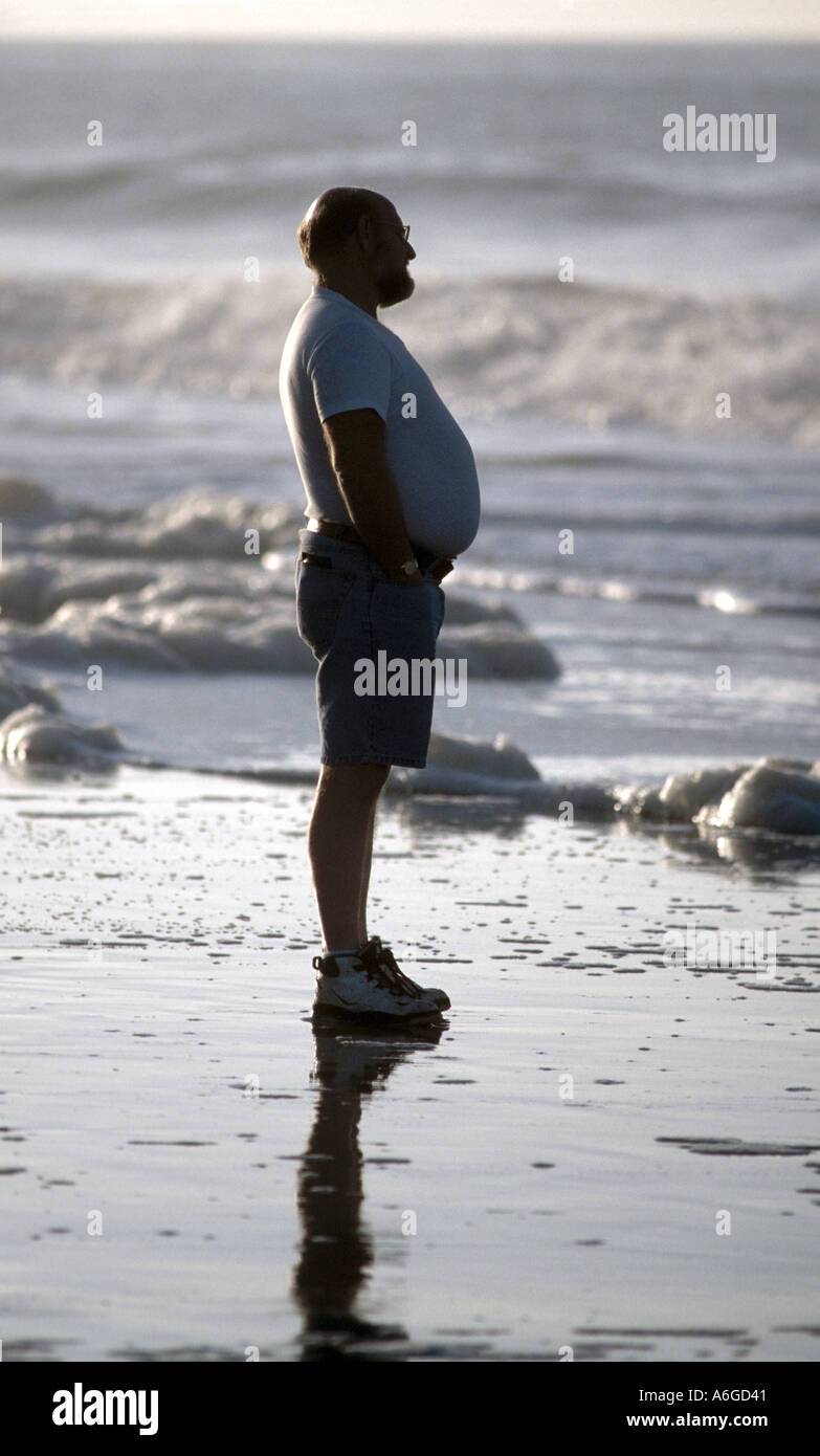 homme blanc d'âge moyen avec gros intestin sur la plage À Myrtle Beach en Caroline du Sud en automne regarder et profiter le surf Banque D'Images