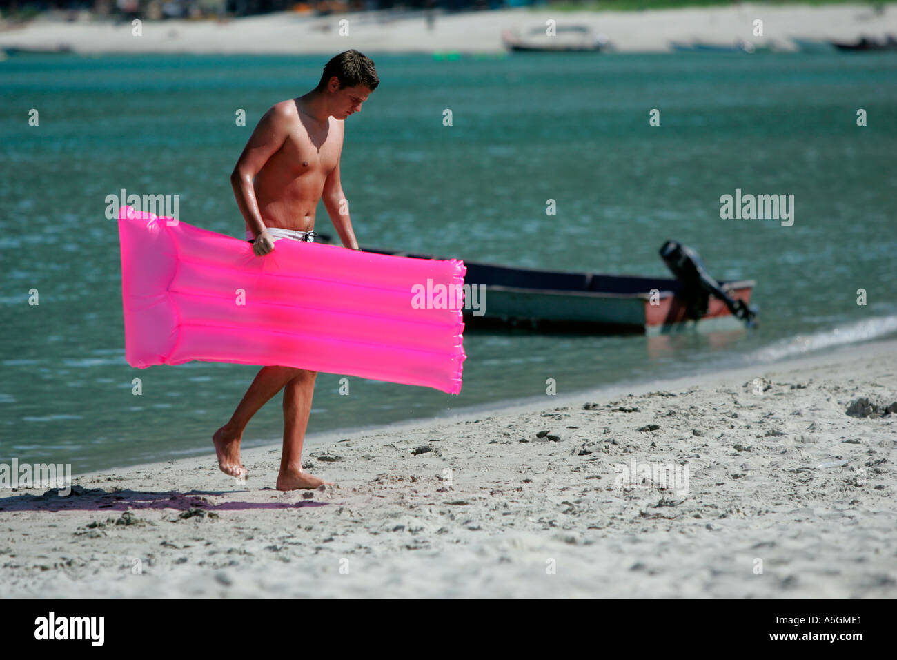 Jeune homme marche jusqu'plage avec matelas d'air rose Perhentian Kecil Malaisie Banque D'Images