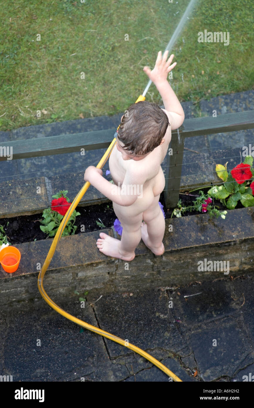 Jeune garçon enfant nu nu nu dans un jardin de banlieue à jouer avec un  flexible NAOH Photo Stock - Alamy