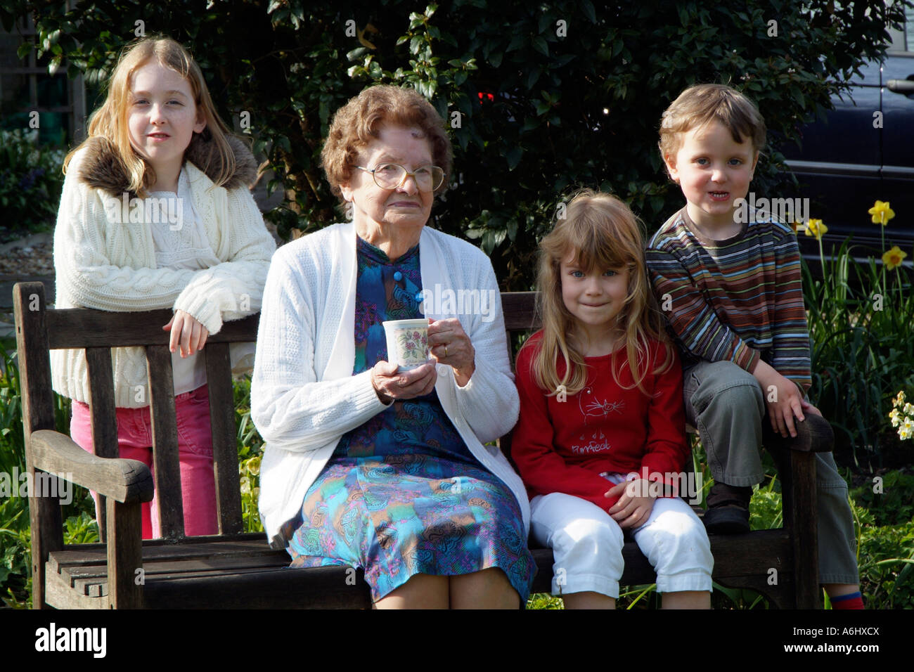 Les enfants de famille avec grand-mère s'asseoir sur un siège de jardin grand-mère tient une tasse de thé Banque D'Images