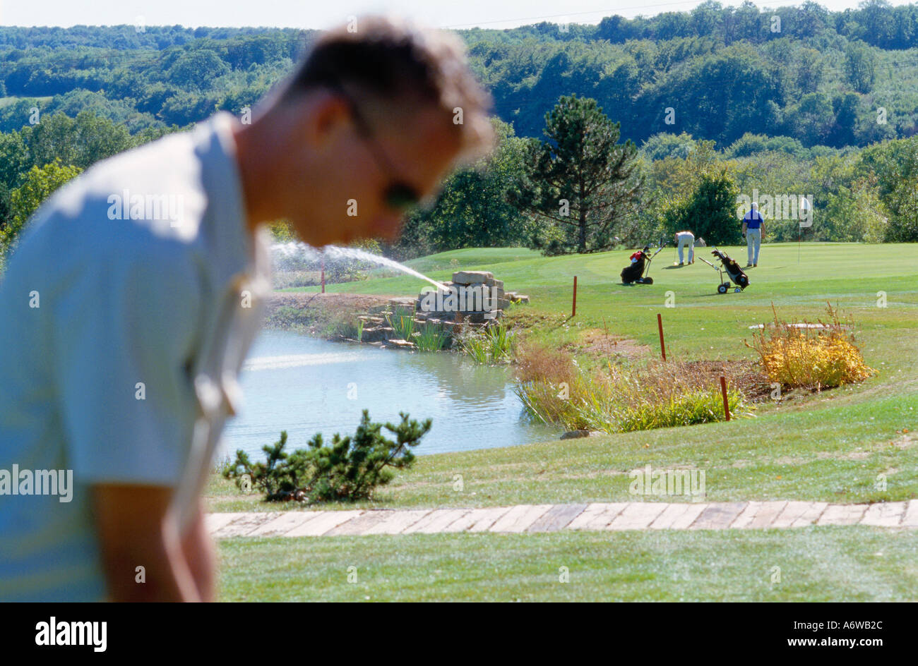 Jeune homme se préparer pour une course de golf avec l'accent sur le contexte où deux autres golfeurs sont visibles Banque D'Images