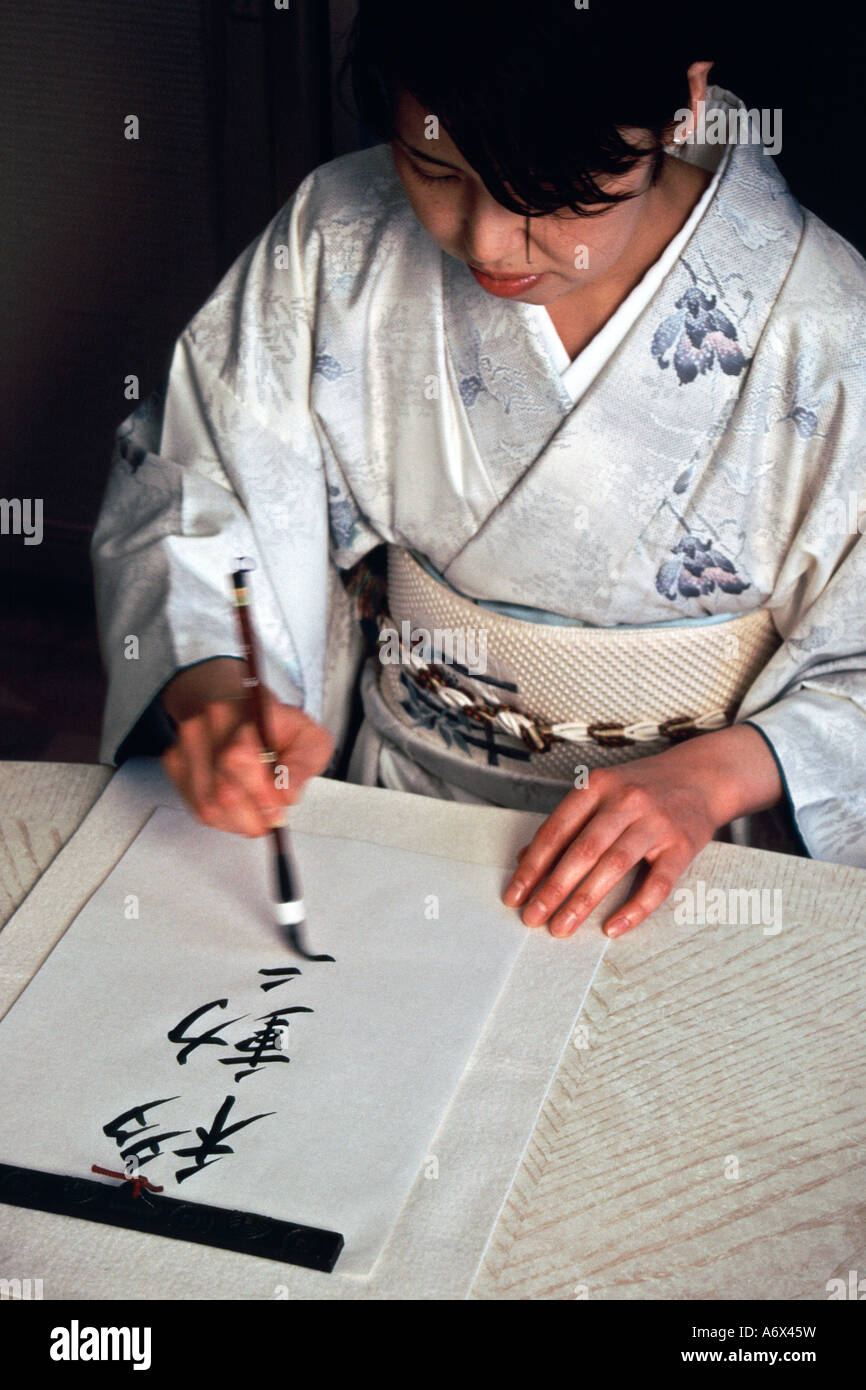 Une dame en kimono japonais écrit en kanji avec un pinceau. Banque D'Images