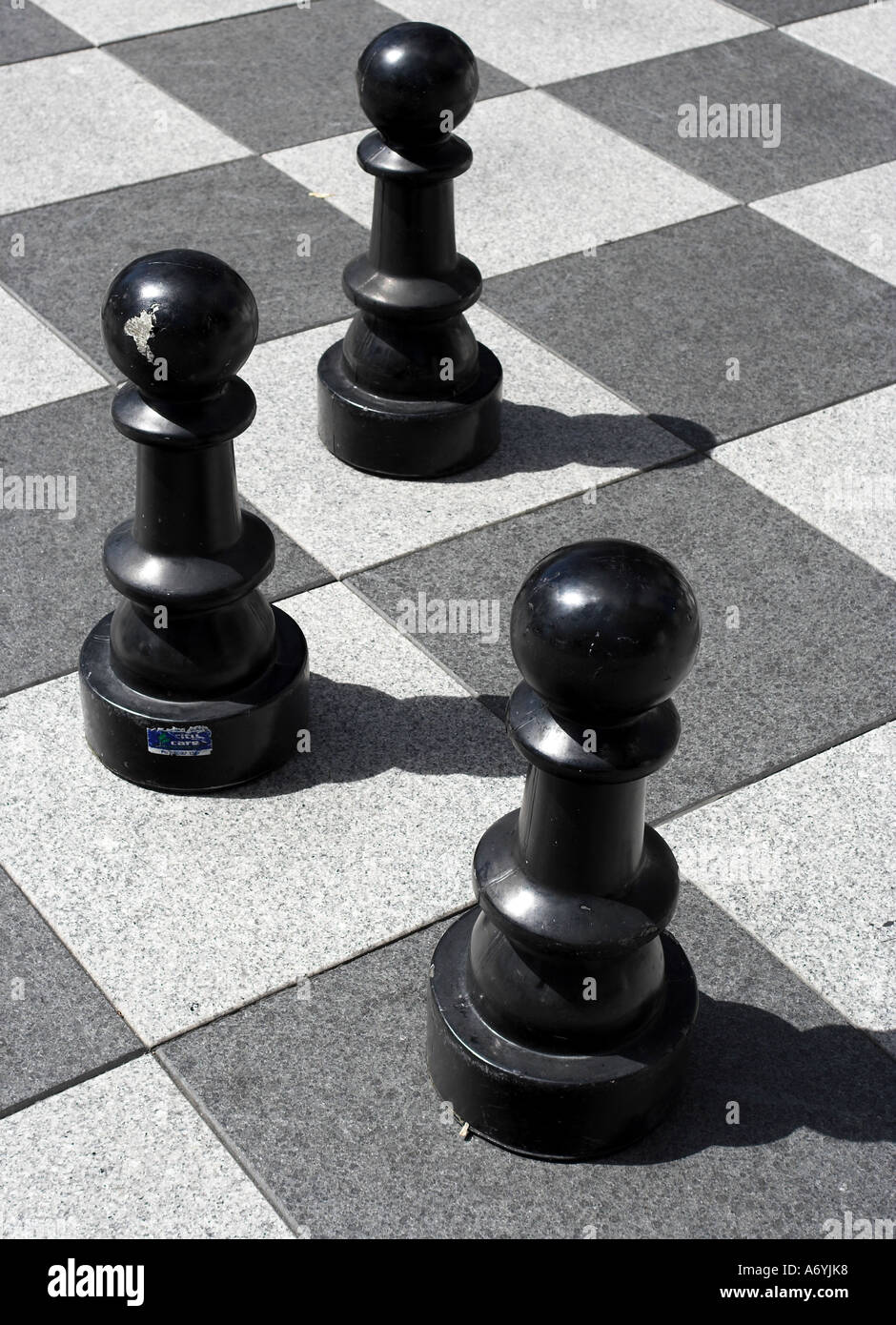Trois échecs noir géant des pions sur un échiquier à l'extérieur du centre-ville. Banque D'Images