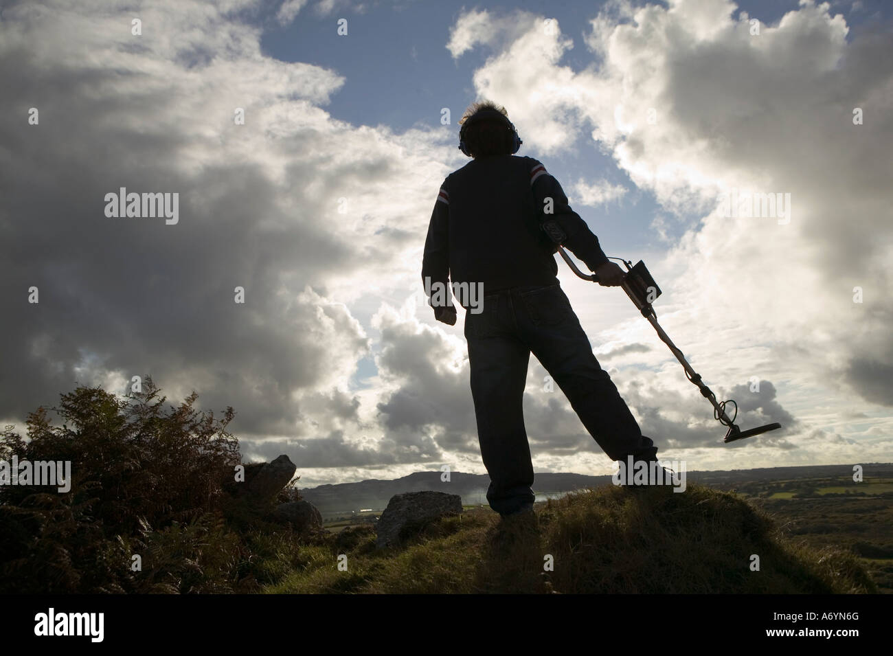 Homme avec détecteur de métal découpé sur le ciel bleu et nuageux. Banque D'Images