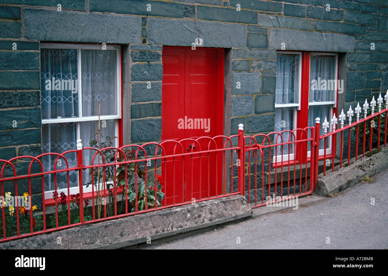 Maison construite à partir de blocs gris rouge vif avec porte avant et garde-corps. Fenêtres à guillotine peint en blanc avec du rouge l'entoure. Banque D'Images