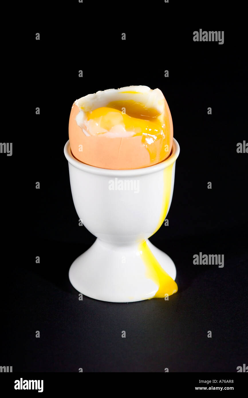 Un œuf dur par un écoulement d'œuf dans un coquetier blanc sur fond noir pur. Banque D'Images