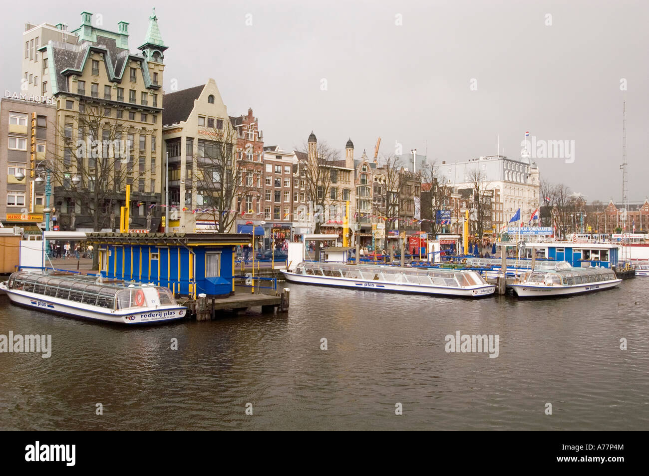 Les bateaux des guides touristiques partent sur le canal près de la rue Damrak à Amsterdam, en Hollande, avec une architecture hollandaise historique et un ciel nuageux. Banque D'Images