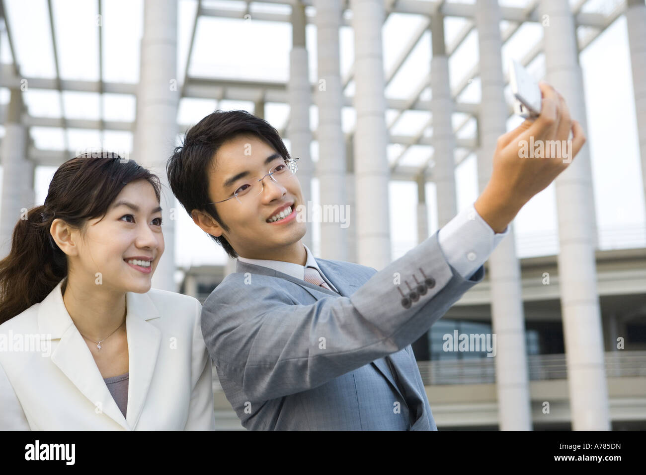 Businessman standing next to female colleague, taking photo with cell phone Banque D'Images