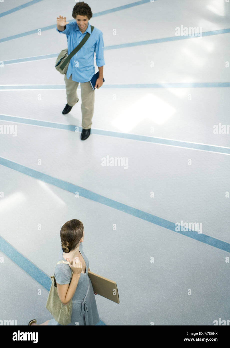 Teenage boy wearing messenger bag waving to amie, pleine longueur, high angle view Banque D'Images