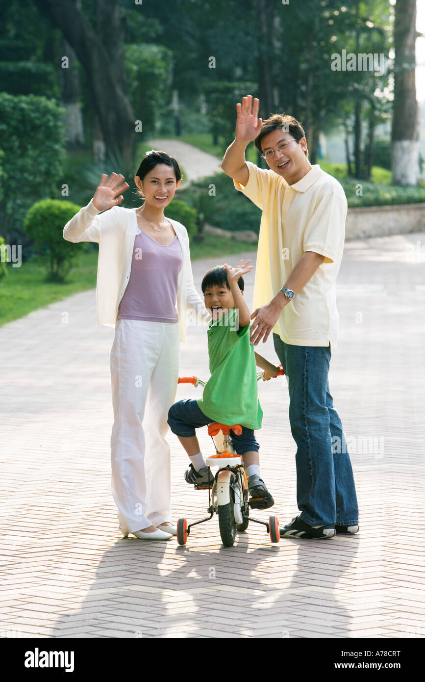 Boy riding bicycle, les parents des deux côtés, en agitant à huis clos Banque D'Images